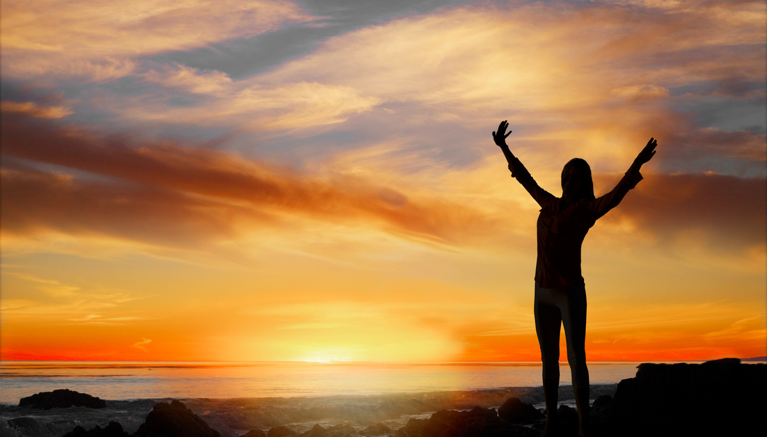 Empowered woman. Woman standing with arms raised near ocean in sunset